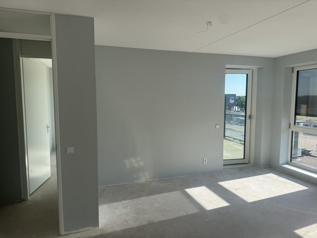 Kamer in een nieuw appartement met balkondeur en egaal gesausde lichtgrijze wanden