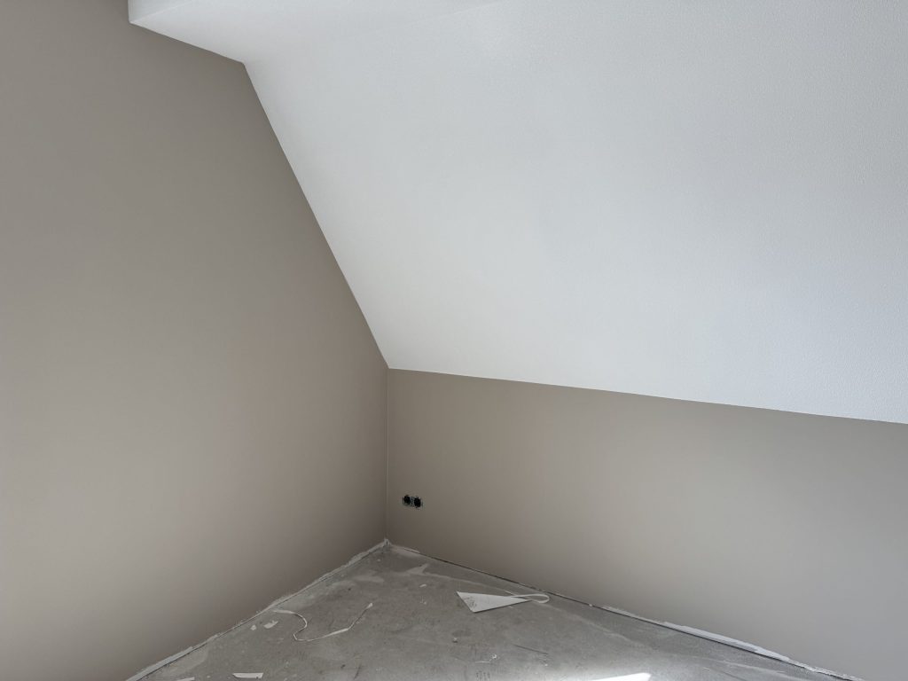 Zolderkamer met schuine wand, strak afgewerkt in een zandkleur met een wit plafond