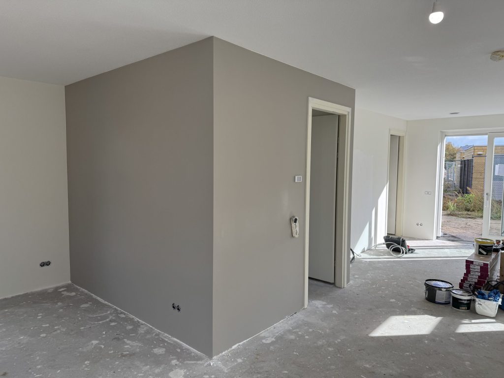 Pas afgewerkte grijze wand in een nieuwbouwwoning, met verfemmers nog op de betonvloer