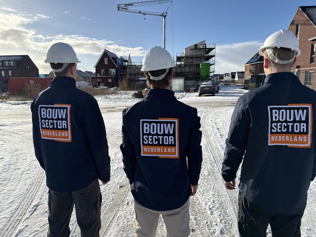 Drie vakmensen van Bouwsector Nederland met witte helm voor een rij woningen in aanbouw
